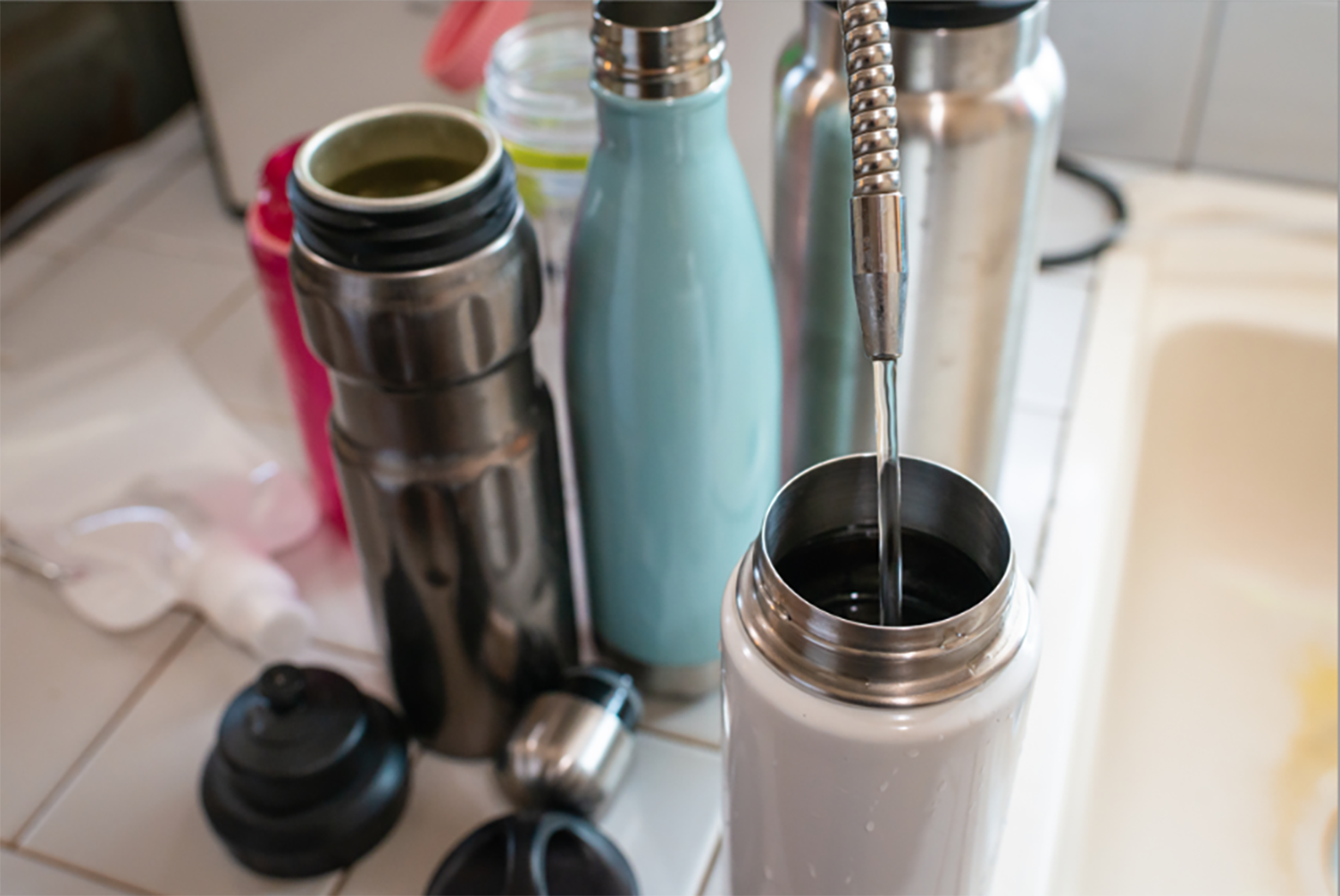 A photo of metal water bottles being filled by a tap.