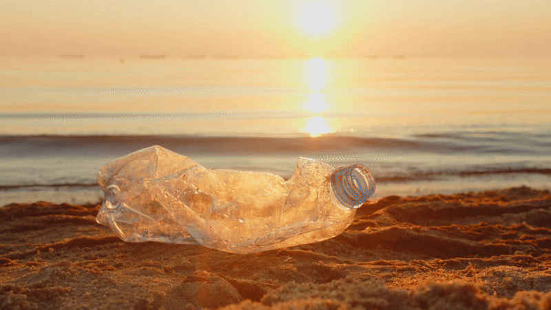 Gif of a crushed plastic bottle on a beach at sunset, picked up by a man walking by collecting trash.